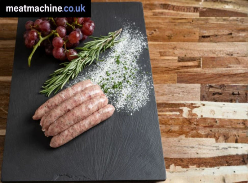 Raw sausages on a slate board with rosemary and grapes on a wooden background, featuring the brand 'meatmachine.co.uk'.
