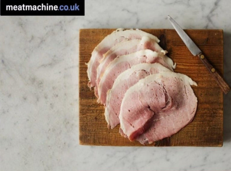 Sliced raw meat on a wooden cutting board with a knife, branded 'meatmachine.co.uk'.