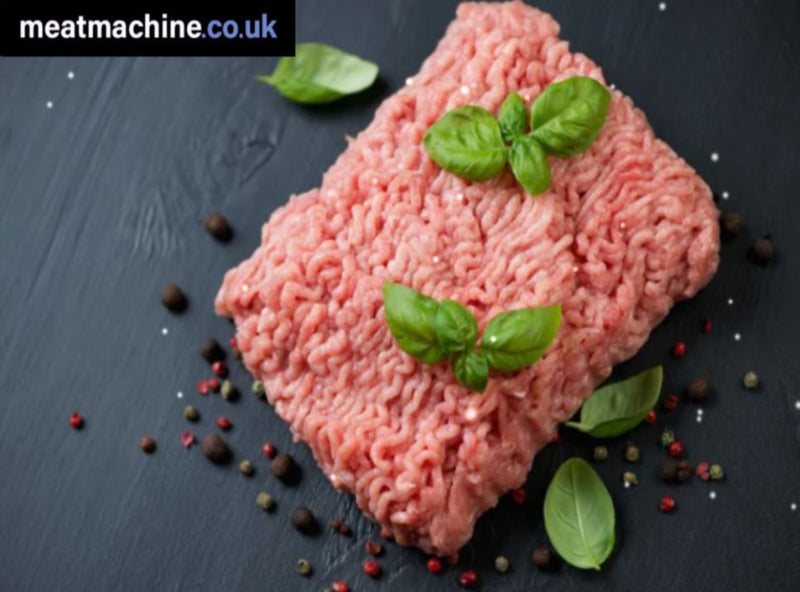 Ground meat with basil leaves on a dark surface, featuring the brand 'meatmachine.co.uk'.
