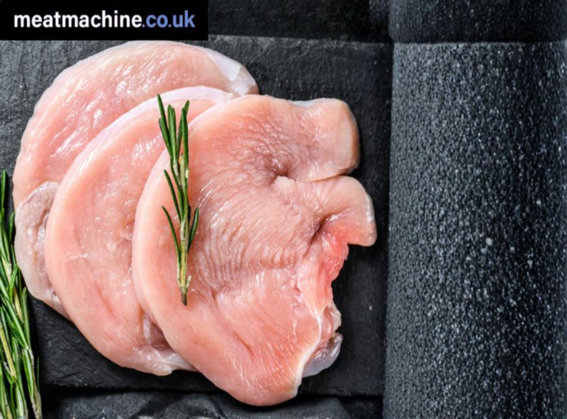 Raw chicken breasts with rosemary on a black slate surface, branded 'meatmachine.co.uk'.