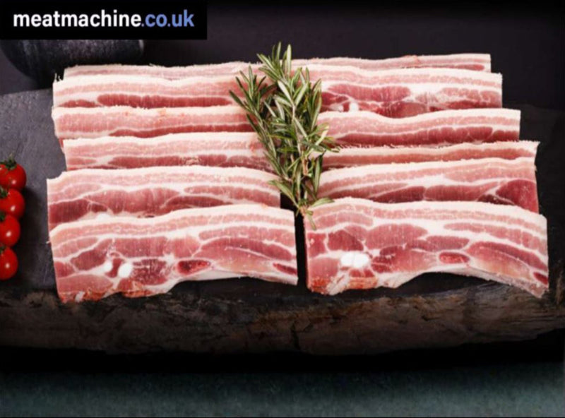 pork belly slices on a wooden board with rosemary and cherry tomatoes, branded 'meatmachine.co.uk'.